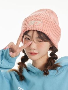 a young woman wearing a pink hat and blue sweatshirt is touching her nose with one hand