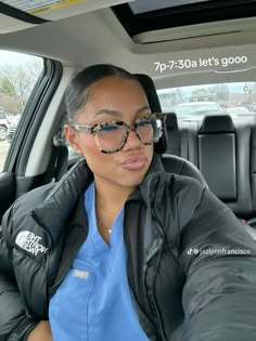 a woman sitting in the passenger seat of a car wearing glasses and a jacket with an onlooker behind her