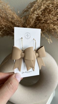 a pair of earrings with bows on them sitting in front of a white card and some dry grass