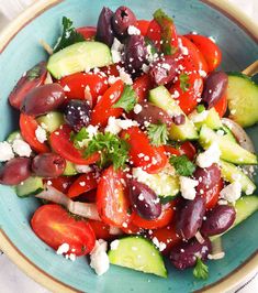 a blue bowl filled with cucumbers, tomatoes and olives topped with feta cheese