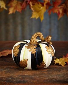 a black and white striped pumpkin sitting on top of a wooden table next to leaves