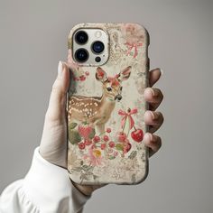 a woman holding up an iphone case with a deer on it's back and flowers in the background