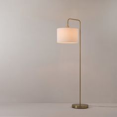 a floor lamp with a white shade on the base and a gold metal frame around it