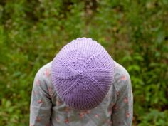 a person wearing a purple knitted hat standing in front of some green bushes and trees