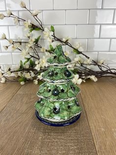 a green glass christmas tree on a wooden table with white flowers and branches in the background