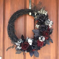 a wreath is hanging on the door with black and red flowers, leaves and feathers