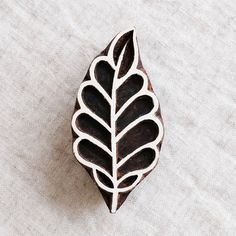 a wooden brooch with a leaf design on it's center piece, sitting on a white surface