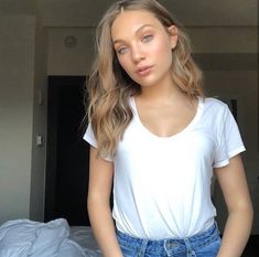 a woman standing in front of a bed wearing a white t - shirt and blue jeans