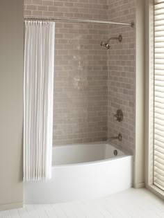 a bath tub sitting under a window next to a shower curtain in a white bathroom