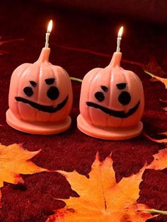 two candles with faces painted on them are sitting in front of some leaves and one candle is lit