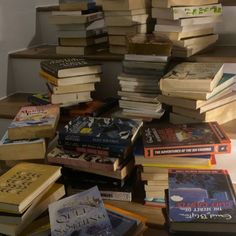 a pile of books sitting on top of a wooden table next to a stair case