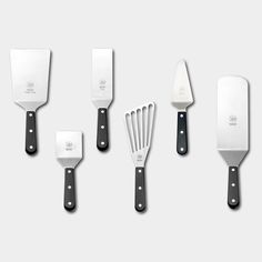 five kitchen utensils are lined up in a row on a white surface with black handles