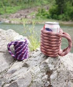 a rope wrapped coffee mug sitting on top of a rock next to a river