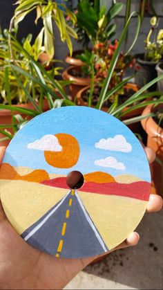 a hand holding up a painted disc with a road going through the center and clouds in the sky