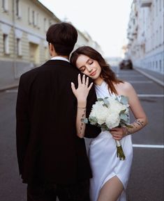 a man and woman standing next to each other in the street with flowers on their arm