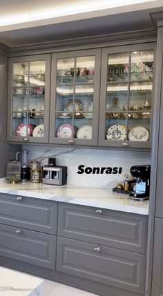 a kitchen with gray cabinets and white counter tops, along with plates on the wall