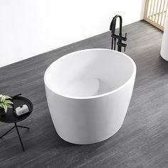 a white bath tub sitting on top of a wooden floor next to a black table