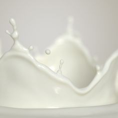 a white liquid splashing on top of it's surface in front of a gray background