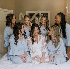 a group of women sitting on top of a bed in matching blue robes and smiling