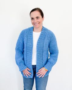 a woman standing in front of a white wall wearing a blue knitted cardigan