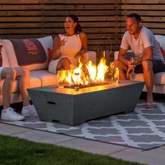 two people sitting on couches in front of a fire pit with lit candles and wine glasses