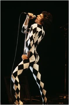 a man in black and white checkered outfit singing into a microphone