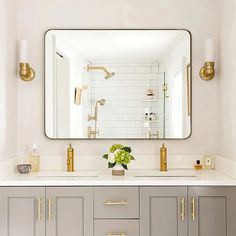 a white bathroom with gold accents and a large mirror over the sink that has a vase on it