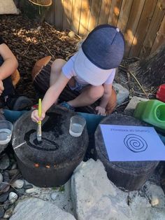 two young boys sitting on the ground in front of buckets filled with water and plants