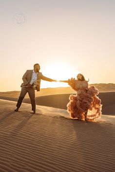 a man and woman dancing in the desert at sunset with their arms spread out to each other