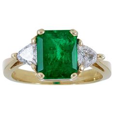 A classic three-stone engagement ring showcasing a color-rich emerald cut green emerald, accented with brilliant trillion (triangular) diamonds on either side. Set in a tapered 18k yellow gold mounting. Emerald weighs 2.59 carats. Diamonds weigh 0.49 carats total. Size 7.5 US (sizable) Dimensions: 0.38 in x 0.68 in. Luxury Trillion Cut Emerald Ring For Formal Occasions, Luxury Gia Certified Trillion Cut Emerald Ring, Luxury Gia-certified Trillion Cut Emerald Ring, Luxury Trillion-cut Emerald Ring, Luxury Trillion Cut Emerald Jewelry, Formal Trillion-cut Emerald Jewelry, Formal Trillion Cut Emerald Ring, Gia Certified Trillion Cut Emerald Rings, Trillion Cut Green Diamond Ring