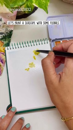 someone is holding a watercolor book and painting it with their hands on the table