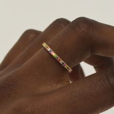 a woman's hand holding a ring with multicolored stones on the band