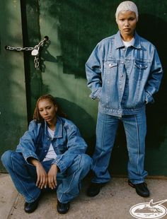 two people standing next to each other in front of a green wall