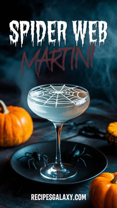 a spider web martini in a coupe glass on a black plate with pumpkins around it