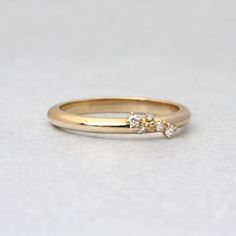 a gold ring with three small diamonds on it's side, sitting on a white surface