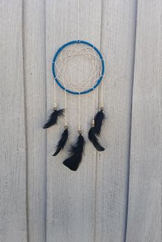 a dream catcher hanging on the side of a wooden fence with black feathers and beads