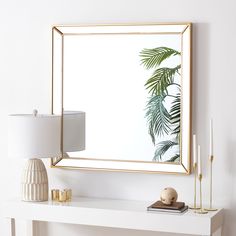 a mirror sitting on top of a white table next to a lamp and a vase