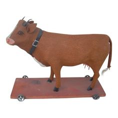 a brown cow standing on top of a wooden board with wheels around it's neck