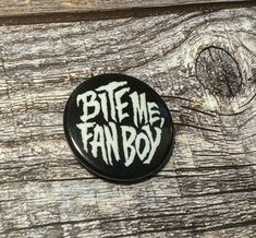 a button with the words bite me fan boy on it sitting on a wooden surface