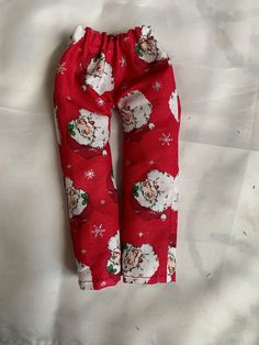 a pair of red pants with santa claus on them sitting on a white sheeted bed