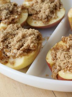 baked apples with crumbled toppings in a white dish on a wooden table