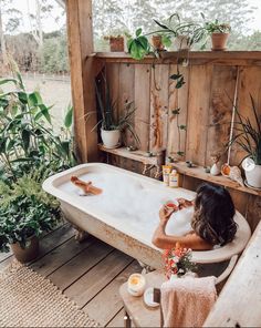 a woman sitting in a bathtub surrounded by potted plants and other greenery