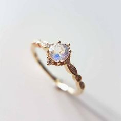 a gold ring with an opal stone and two diamonds on the side, sitting on a white surface