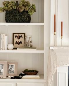 a shelf with pictures, candles and other items on it in a room that has white walls