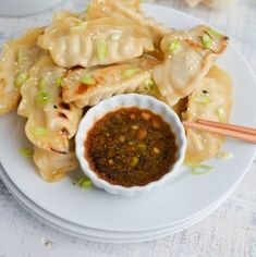 a white plate topped with dumplings covered in sauce and vegetables next to chopsticks