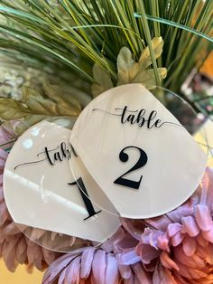 two table numbers are placed on top of each other in front of purple flowers and greenery