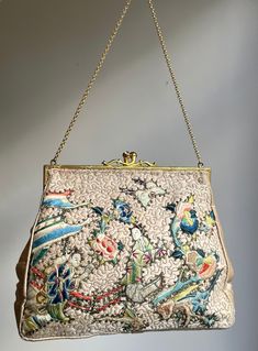 A beautiful 1950s Chinese evening bag. With appliquéd hand-embroidered people, butterflies and roses to the front on a background of embroidered freestyle stitching.   Satin body, once a shell pink colour, now discoloured.  Further freestyle embroidery at the back.  Lovely decorative gold tone frame and a clasp set with two rhinestones.  Lined with satin, edged with fine metallic gold trim. There are two side pockets, one containing a satin-framed mirror. Hangs on a nice chain.  Measurements: 18 Embroidered People, Freestyle Embroidery, Shell Pink, Framed Mirror, Cloche Hat, Embroidered Bag, Pink Colour, Clutch Handbag, Vintage Accessories