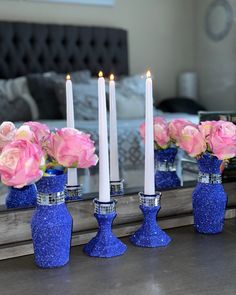 three blue vases with pink roses in them are sitting on a table next to a mirror