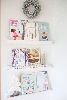 three white shelves with books on them and a wreath hanging from the wall behind them