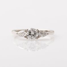 an engagement ring with three stones on the side and one stone in the middle, sitting on top of a white surface